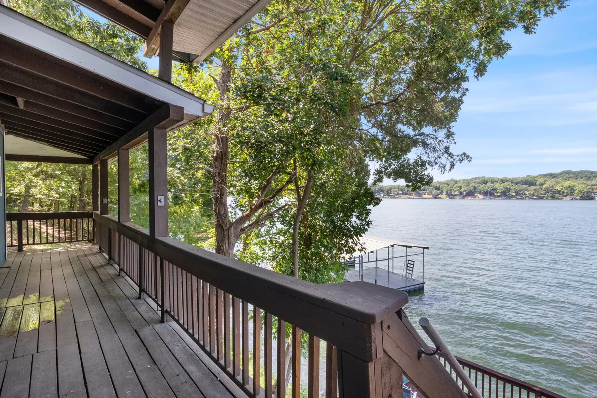 A serene lakeside deck surrounded by trees, looking directly out over calm water. The wooden deck offers a tranquil spot for relaxing, with the lake and nature as the central focus.