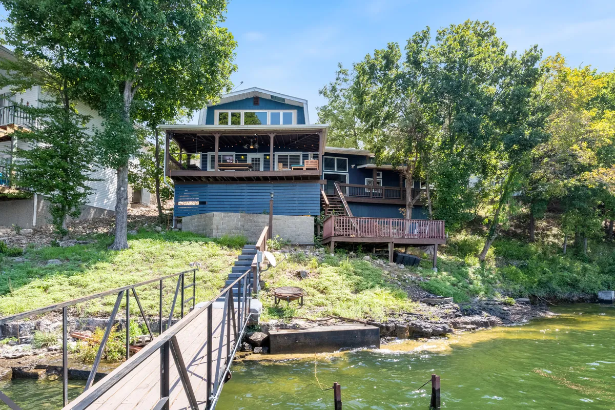 A wide shot of the house with large windows, a spacious wooden deck, and a pathway leading towards it, all surrounded by greenery. The setting is welcoming, showcasing how close indoor comfort is to outdoor exploration and nighttime adventures.