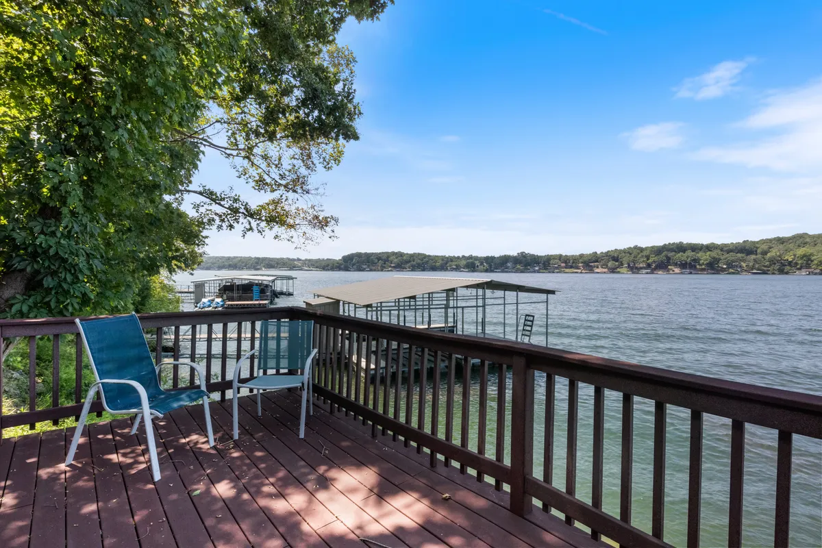 A beautiful wooden deck overlooks the tranquil lake, surrounded by lush trees. Comfortable lounge chairs are arranged for sunbathing or relaxing, offering stunning views of the water. The expansive deck area is perfect for unwinding or gathering with friends, with the lake just steps away.
