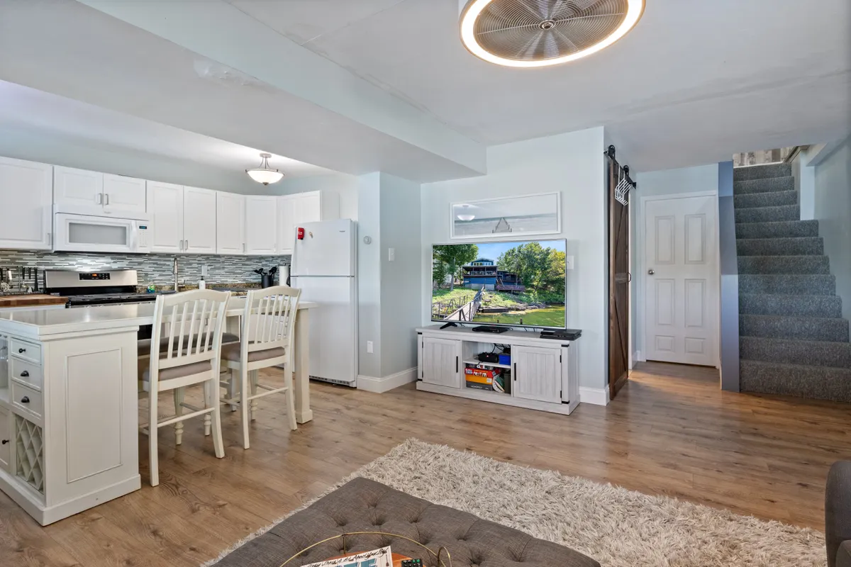 A cozy, open-plan area showing the kitchen island, dining chairs, a television area, and a staircase. The space is arranged for easy flow between cooking, dining, and relaxing, ideal for group meals or hosting family and friends.