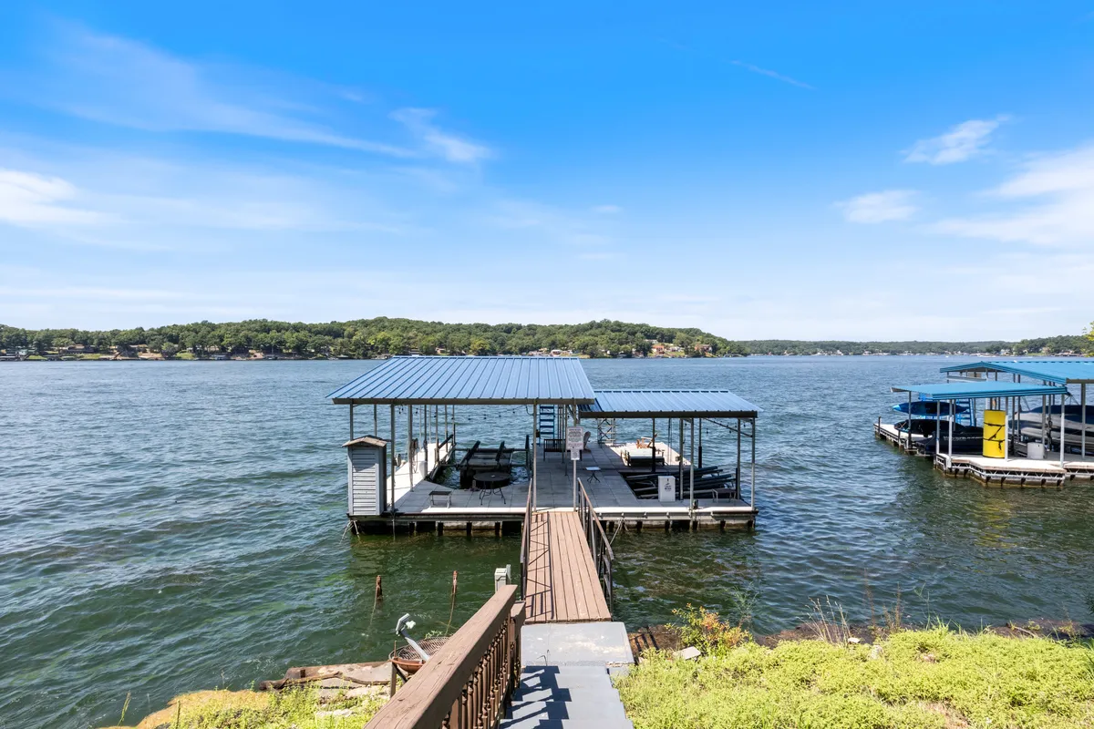 A picturesque dock extends over the water, surrounded by a lush tree line. Several boats are moored at the dock, hinting at easy access for boating or fishing adventures. The tranquil water and inviting seating areas make this a perfect spot for gathering with friends, watching sunsets, or preparing for a day out on the lake.