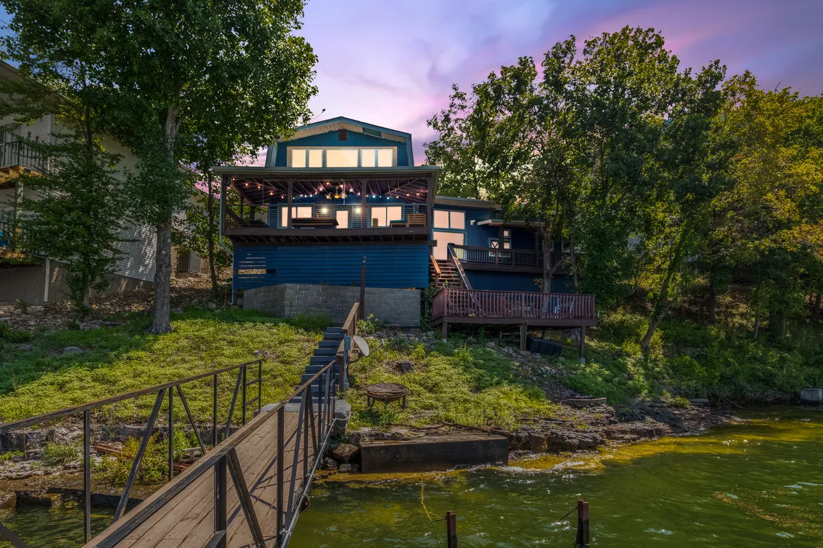 A broad view of the property showcases both the house and its dock jutting out into the sparkling water. The scene captures the lakefront orientation and the seamless connection from home to dock, ideal for launching boating or PWC adventures.