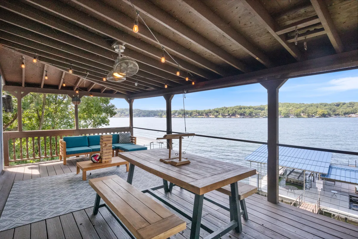 The hero image showcases a spacious wooden deck overlooking the shimmering water, set with a dining table and comfortable seating area. The scene is bathed in the golden hues of sunset, inviting guests to relax, dine al fresco, and soak in the tranquil waterfront atmosphere.