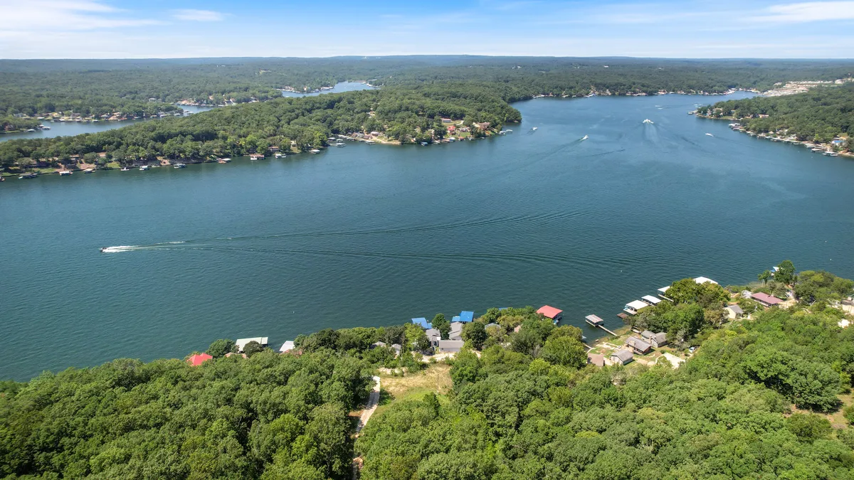 A wide, panoramic view of the expansive lake, bordered by lush greenery and scattered homes along the shoreline. The image suggests numerous water and land activities available in the area.